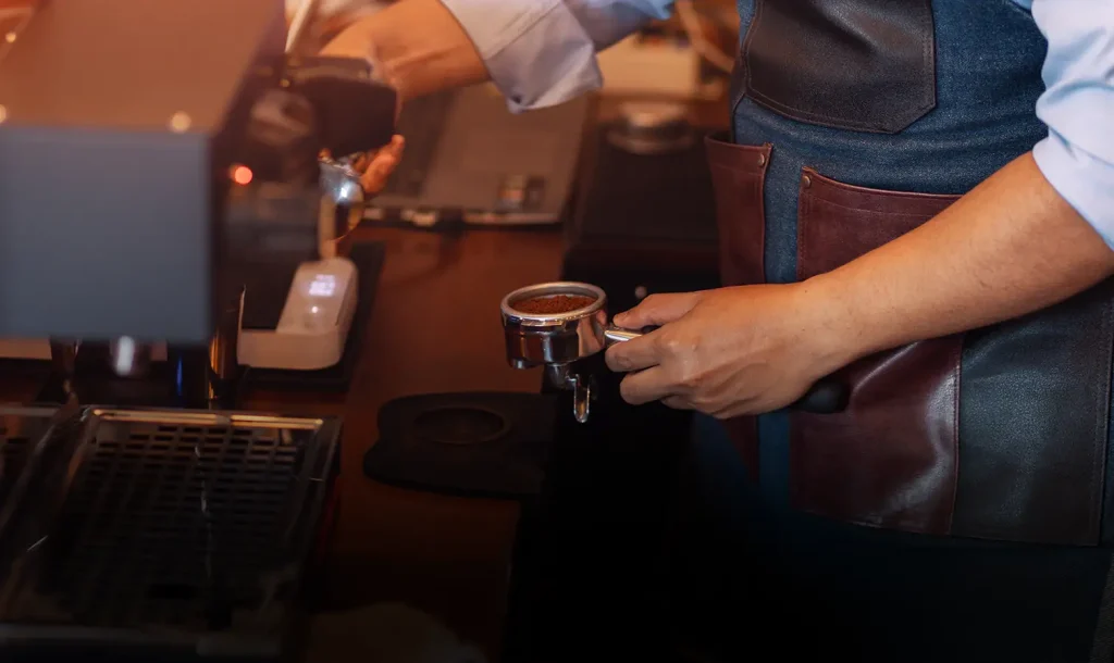 Barista sedang menyiapkan kopi menggunakan mesin espresso sebagai ilustrasi brand kopi lokal yang mengurus perizinan BPOM dan NIB dengan dukungan virtual office.