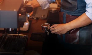 Barista sedang menyiapkan kopi menggunakan mesin espresso sebagai ilustrasi brand kopi lokal yang mengurus perizinan BPOM dan NIB dengan dukungan virtual office.